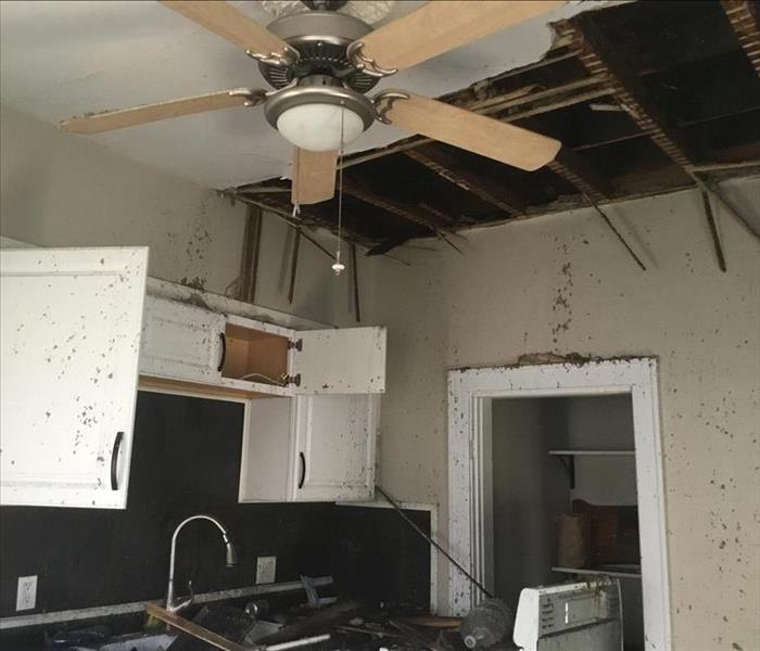 Room with a ceiling fan and half of the ceiling gone. There is soot scattered everywhere.